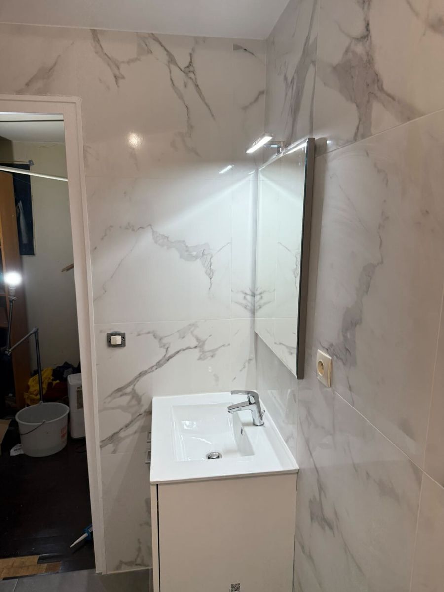 Meuble vasque blanc et miroir dans une salle de bain rénovée avec faïence effet marbre au Vésinet