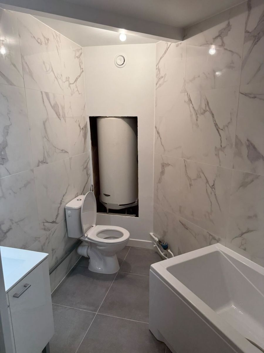 Vue d'ensemble d'une salle de bain rénovée au Vésinet : WC, chauffe-eau en niche, baignoire et meuble vasque
