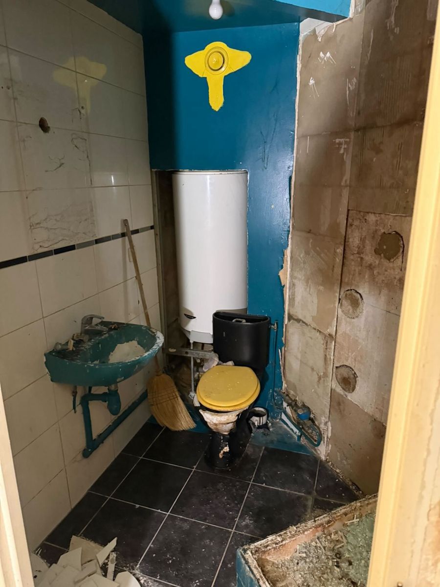 Ancienne salle de bain avant rénovation au Vésinet : carrelage blanc à frise, lavabo et WC bleus, chauffe-eau apparent