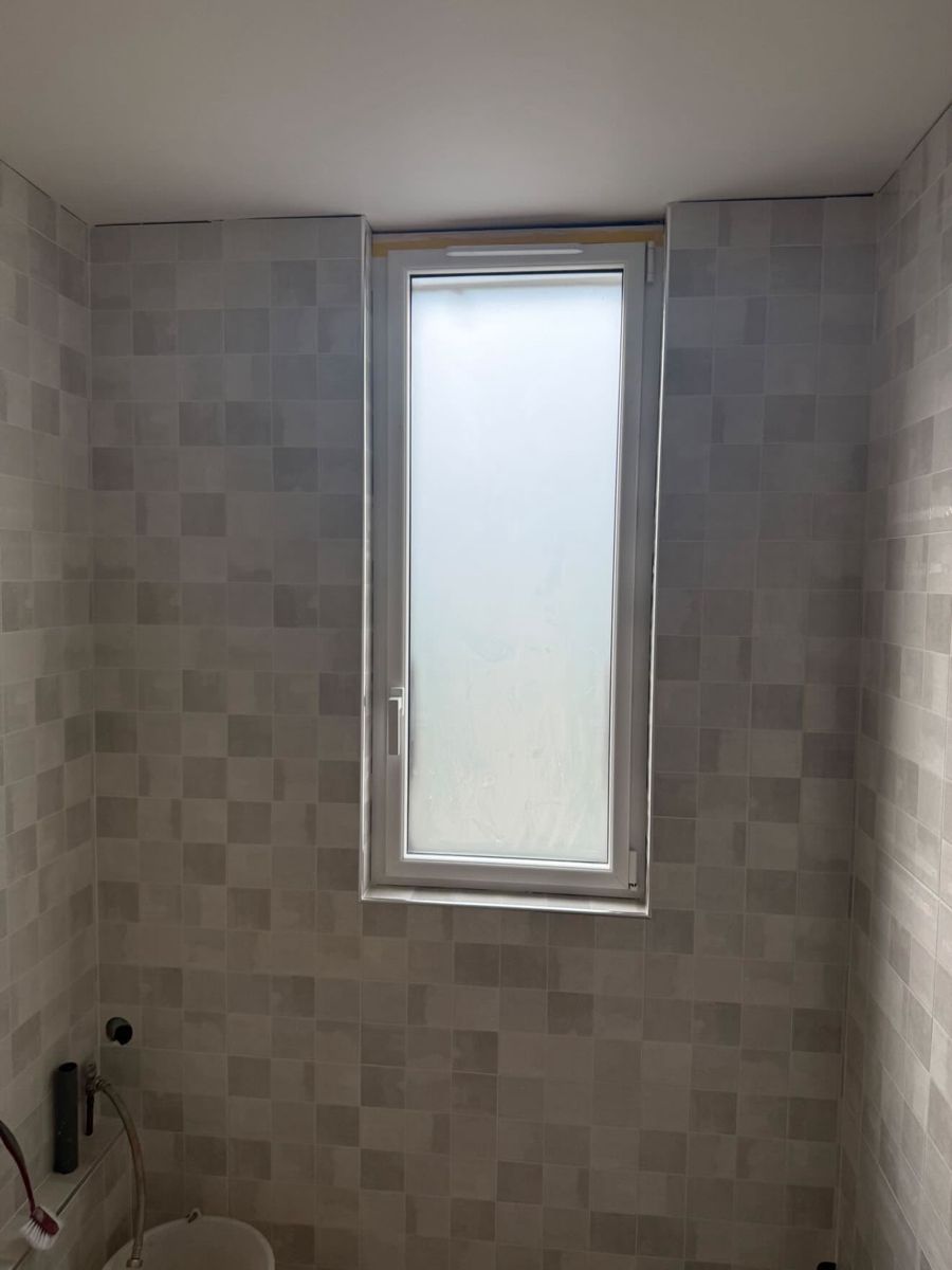 Fenêtre neuve à vitrage dépoli et carrelage zellige dans une salle de bain en rénovation